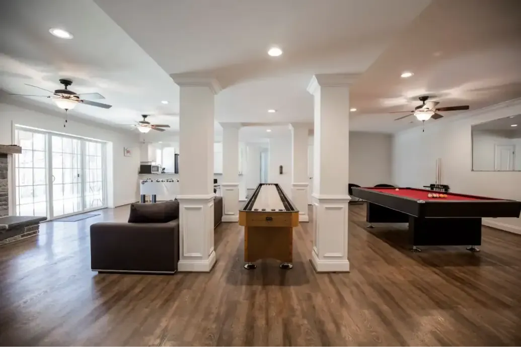 Spacious open-plan recreation room with pool table, leather sofa, and ceiling fans on wood floors.