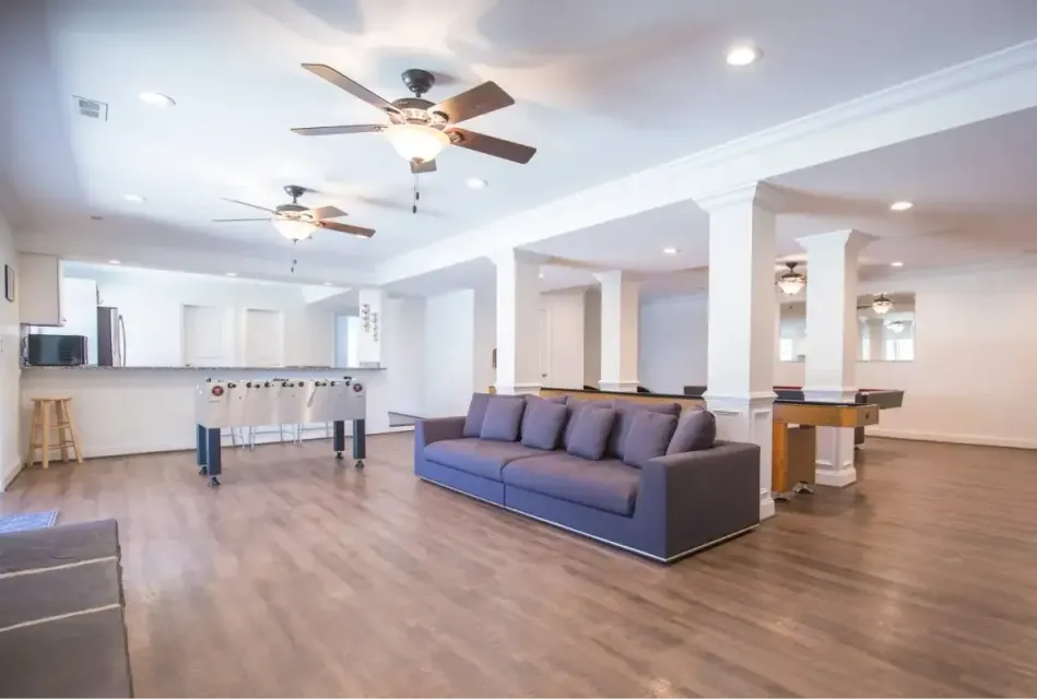 Spacious open-concept living room with a dark blue sofa, ceiling fans, wood floors, and a kitchen bar area