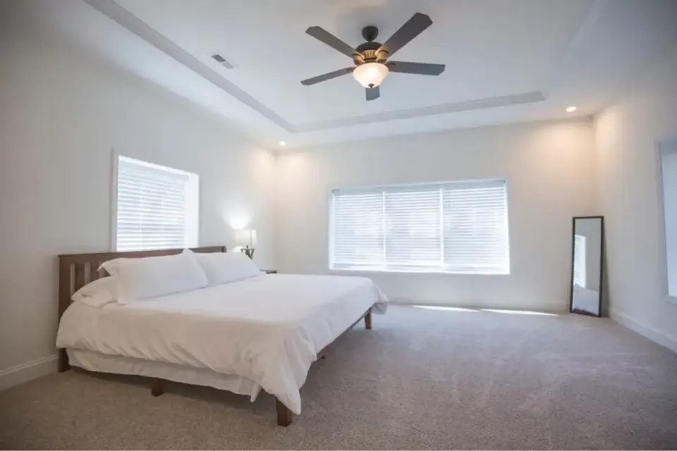 Bright modern bedroom with a bed, ceiling fan, large window, and floor mirror.