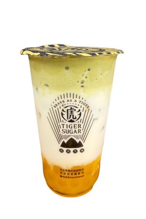 Tiger Sugar brown sugar boba drink with milk being poured, dark boba, and scattered sugar cubes.
