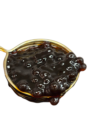 Dark brown boba pearls in a gold spoon. Some pearls are spilling over the side.
