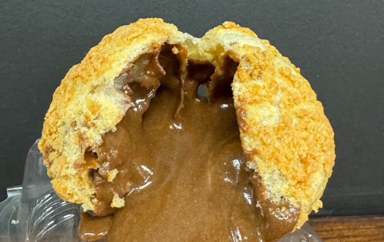 Chocolate cream puff, cut open to reveal rich, flowing filling; golden crust.