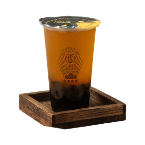 Tiger Sugar drink in a plastic cup with tapioca pearls, on a wooden tray.