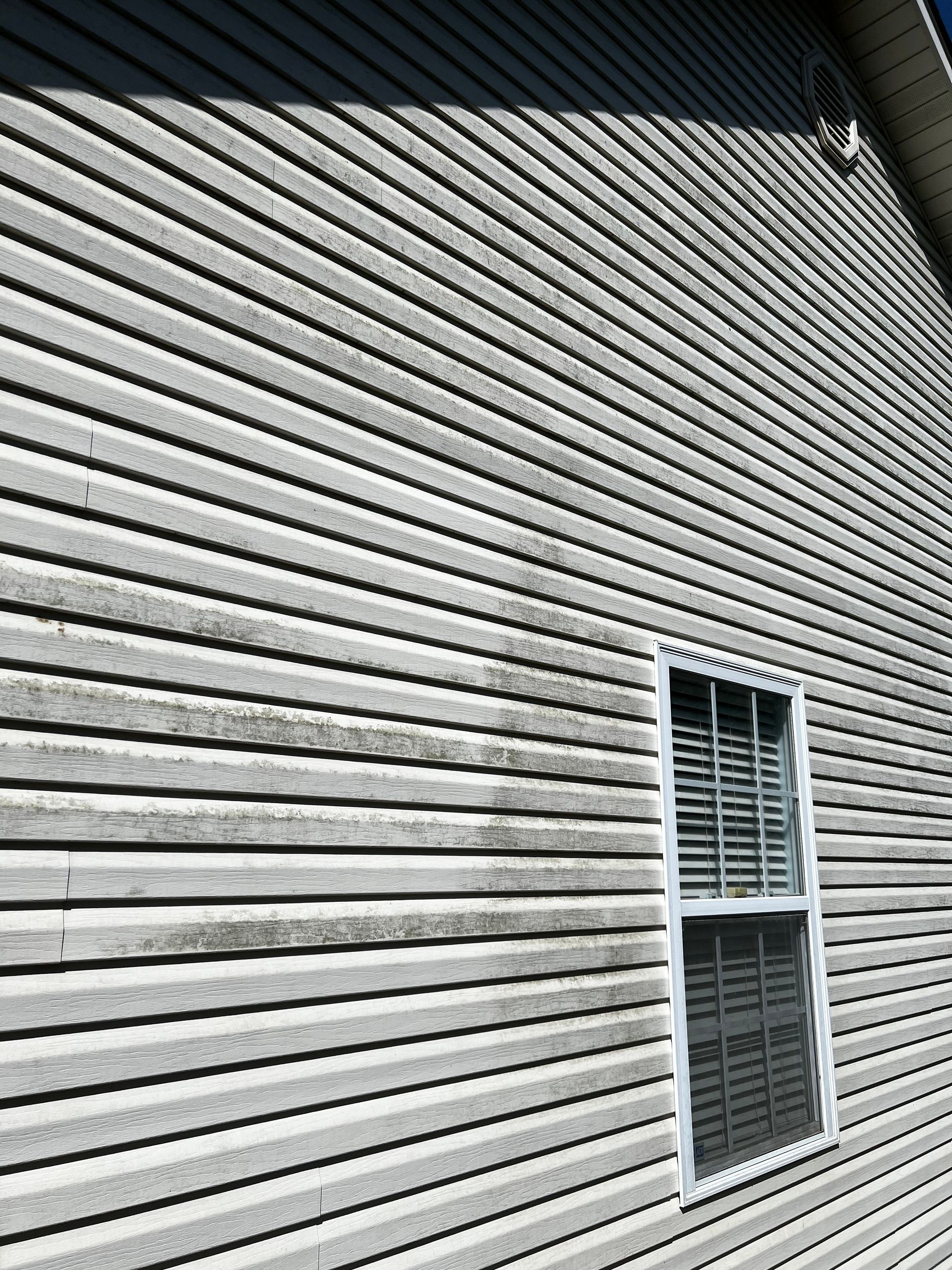 A dirty siding on a house with a window.Job done by 865 Power Wash