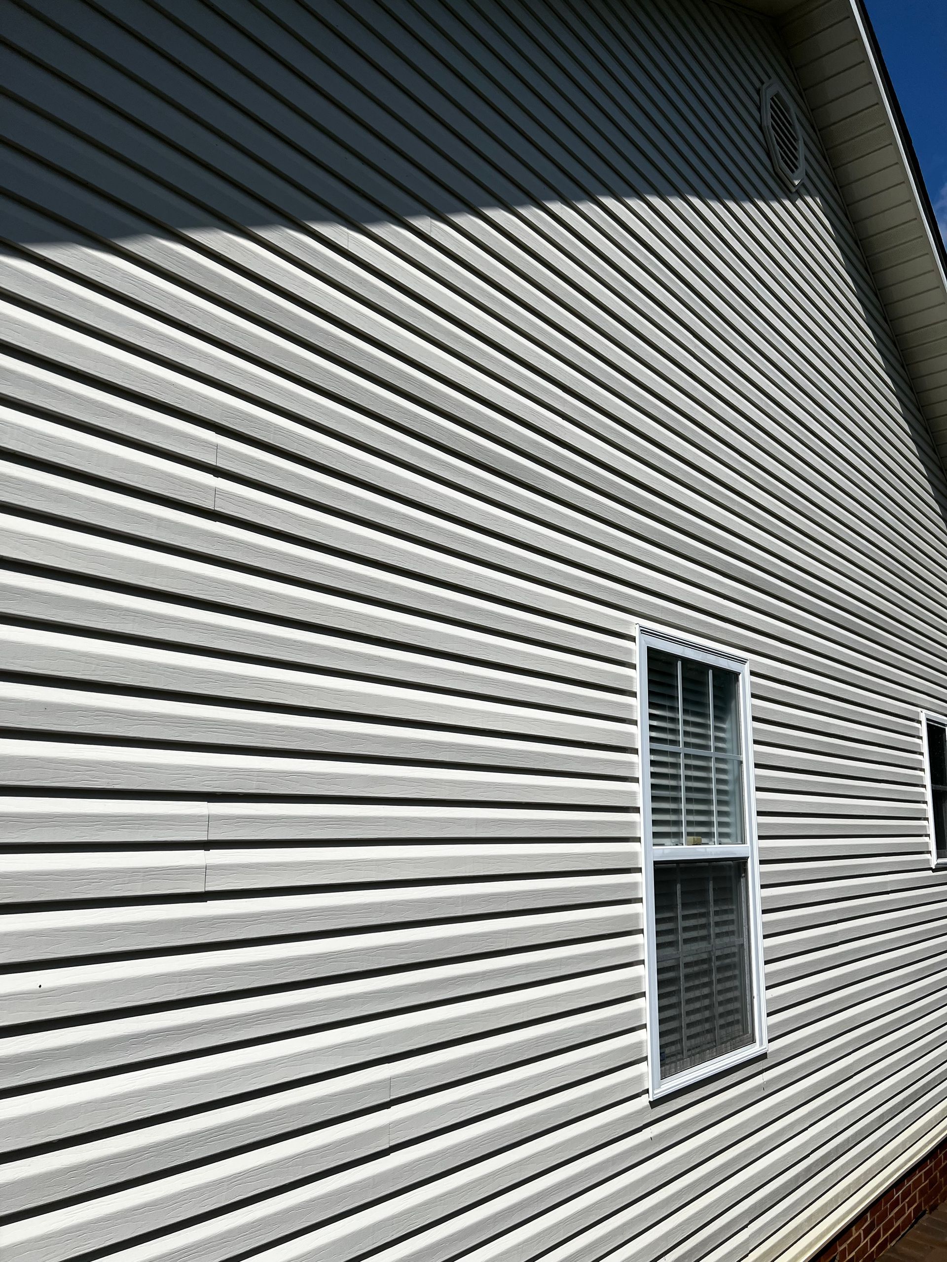 The side of a house with white siding and two windows.Job done by 865 Power Wash