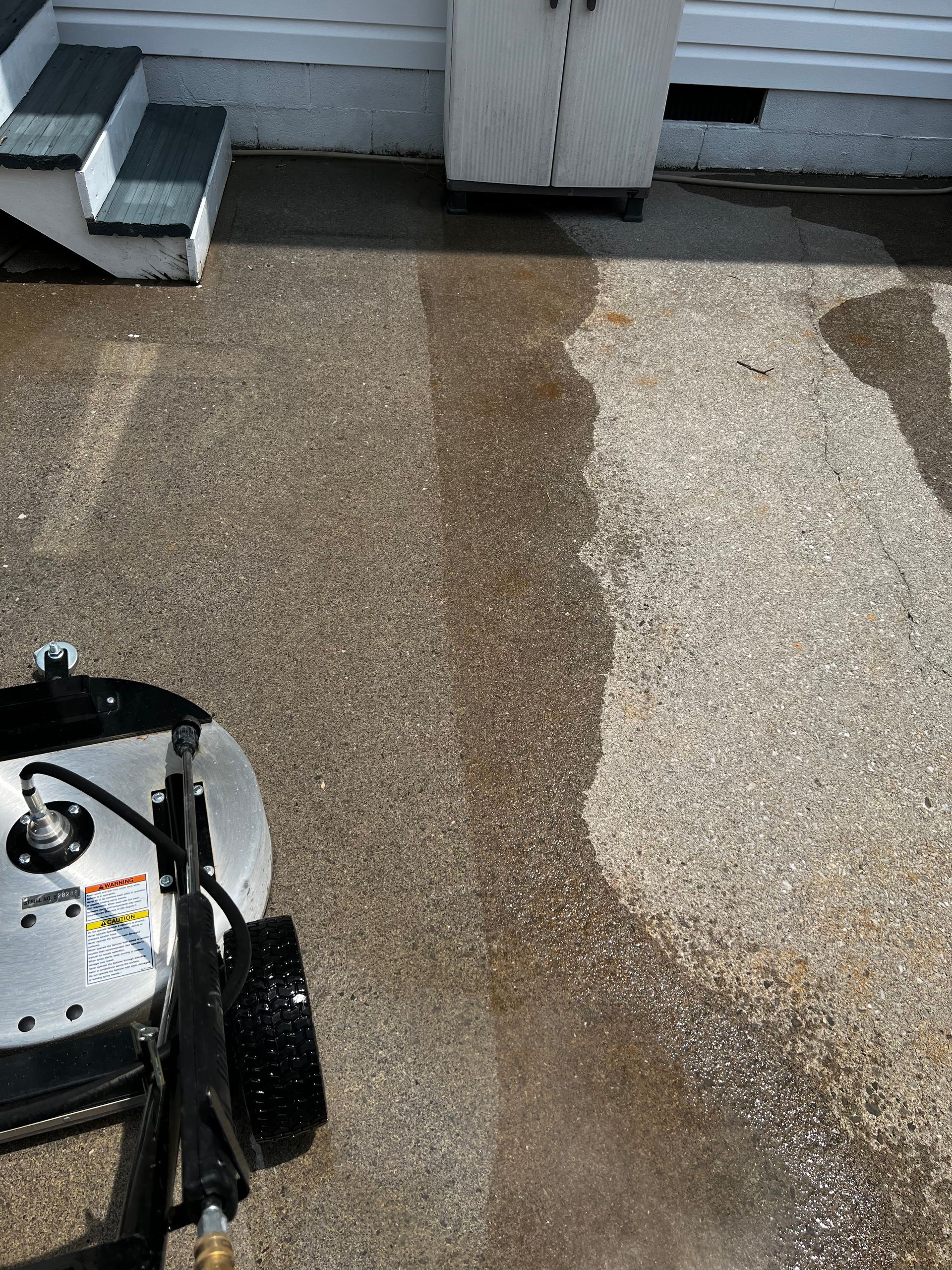 A machine is cleaning a concrete driveway in front of a house.