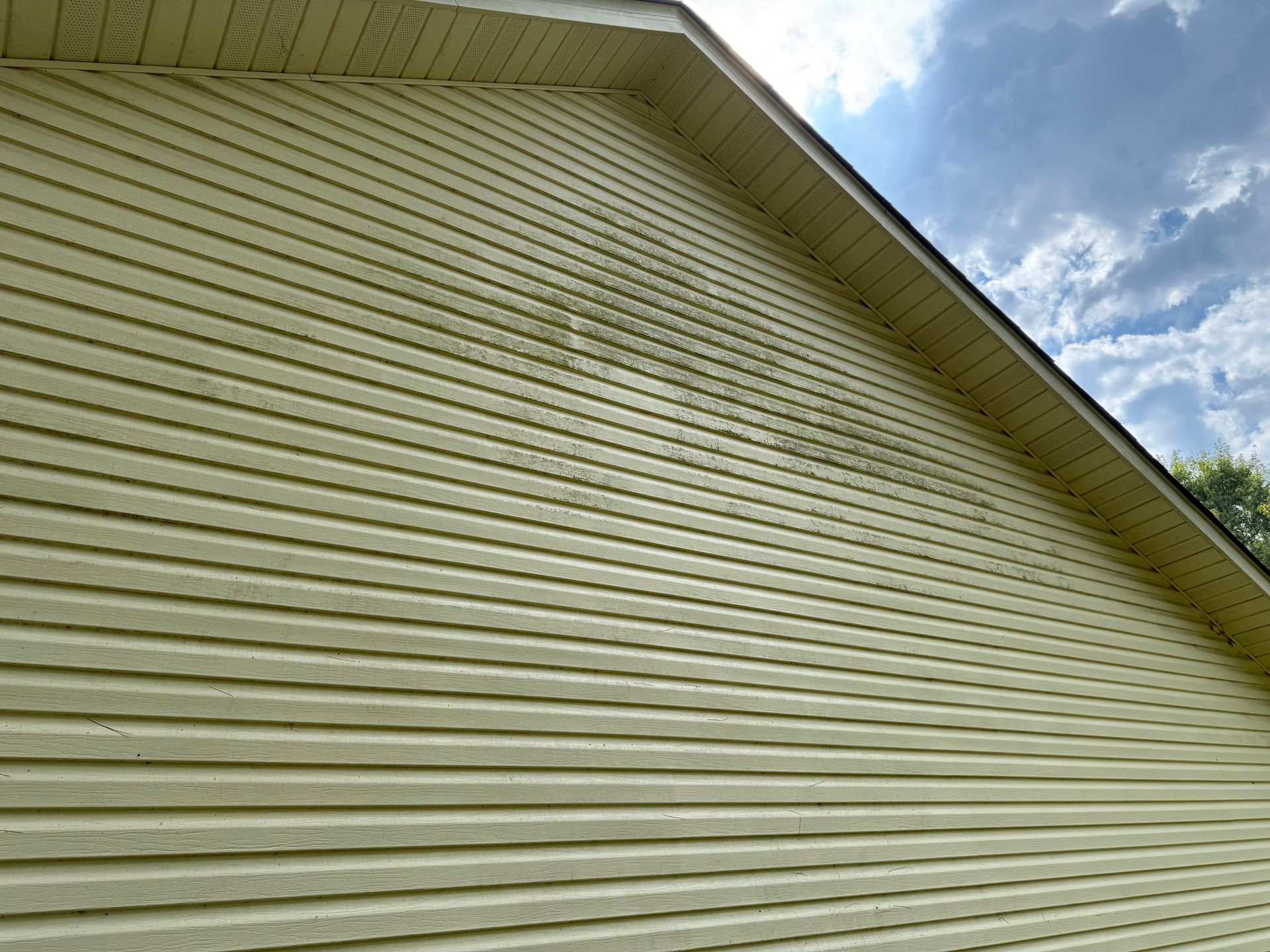 A close up of a yellow house with a roof Job done by 865 Power Wash