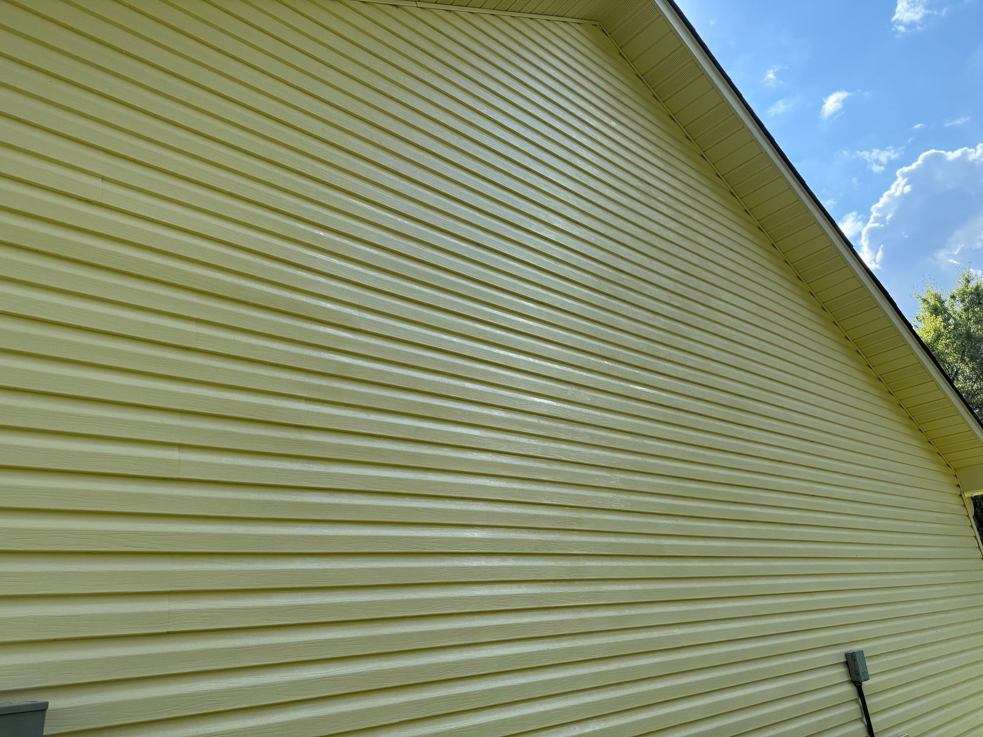 The side of a house with yellow siding and a blue sky in the background. v