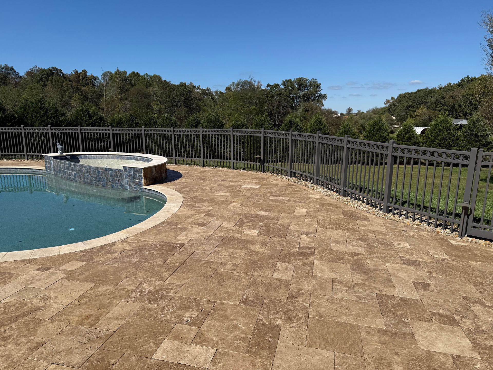 A swimming pool with a fence around it and a hot tub in the background. Paver sealed by 865 Power Wash