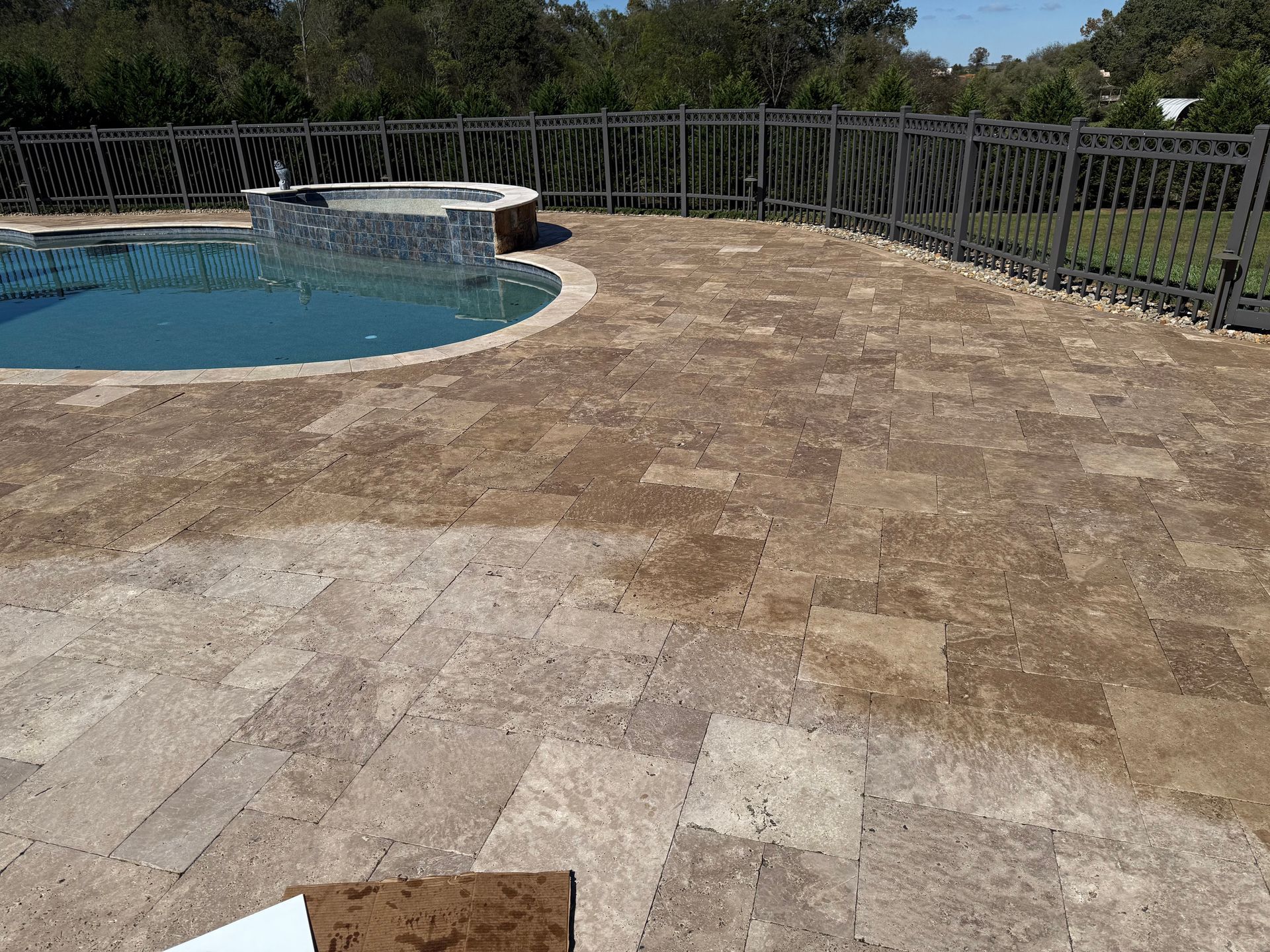 A swimming pool surrounded by a tiled patio and a fence. Paver sealed by 865 Power Wash