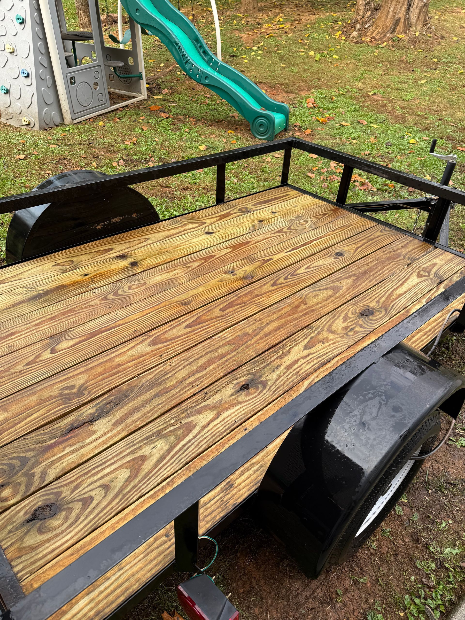 A wooden trailer is parked in a yard next to a slide.