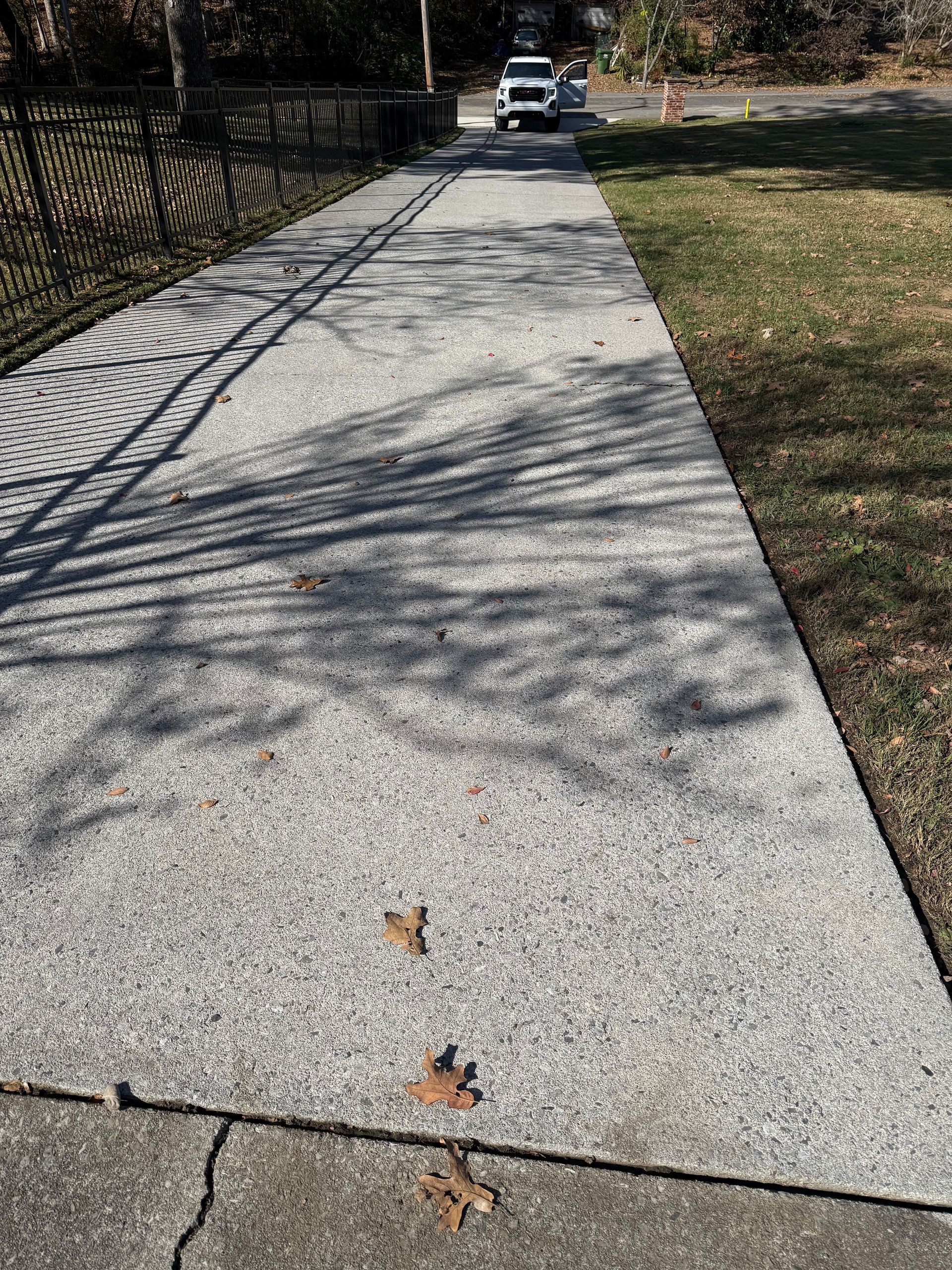 A concrete sidewalk with leaves on it and a car parked on the side of the road.Cleaning by 865 Power Wash