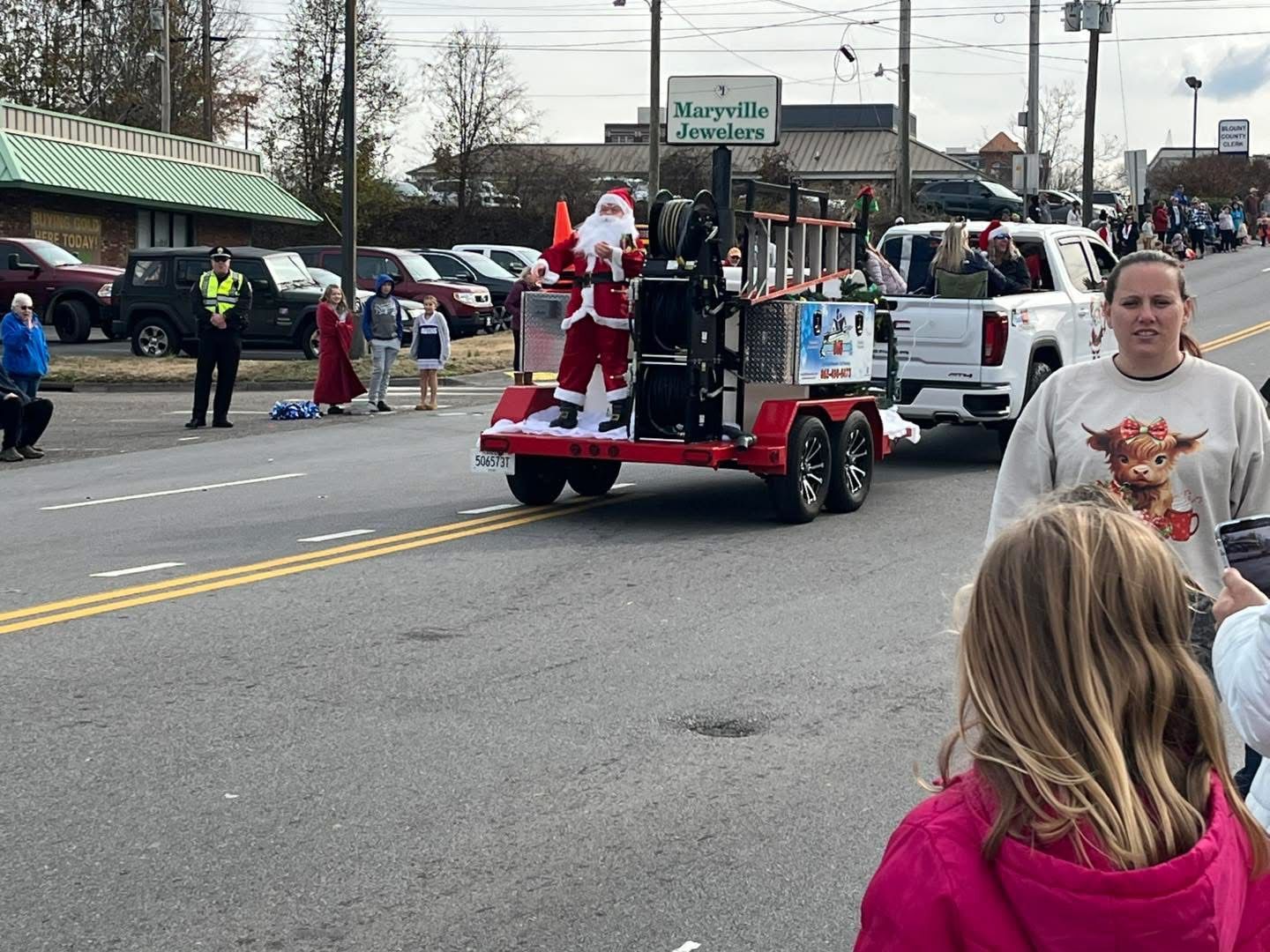 A group of people are watching a parade with santa claus on a trailer.