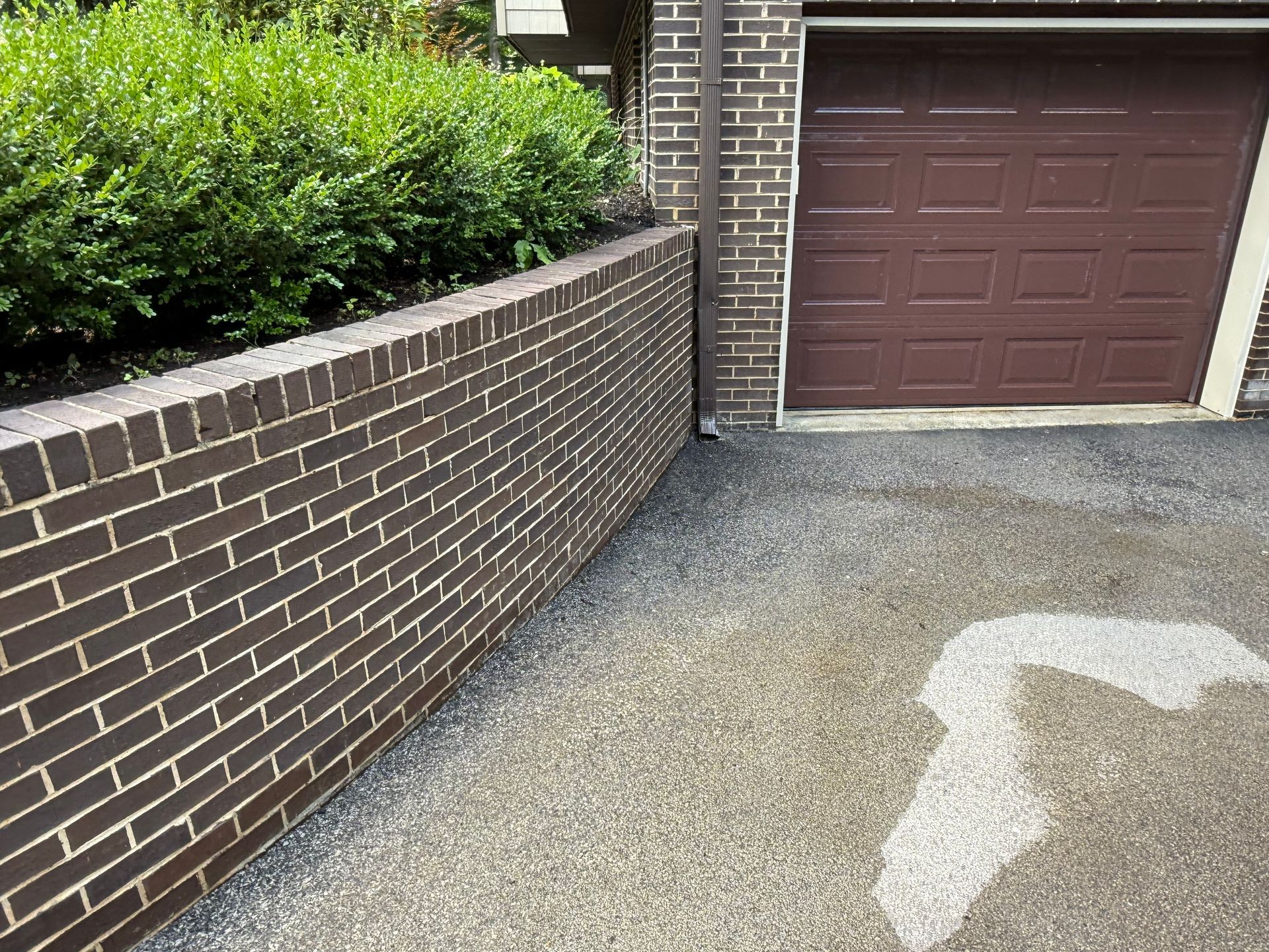 Brown brick retaining wall with green shrubbery and a brown garage door.