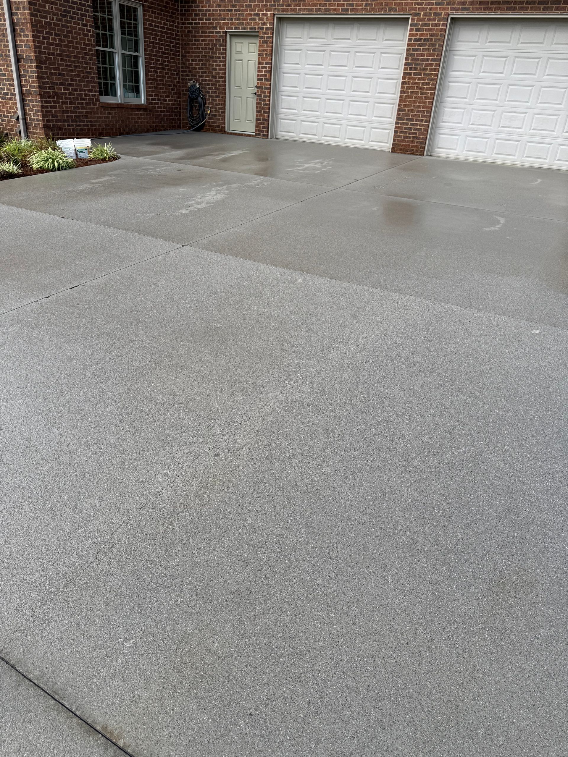Wet asphalt driveway in front of a brick house with two white garage doors.