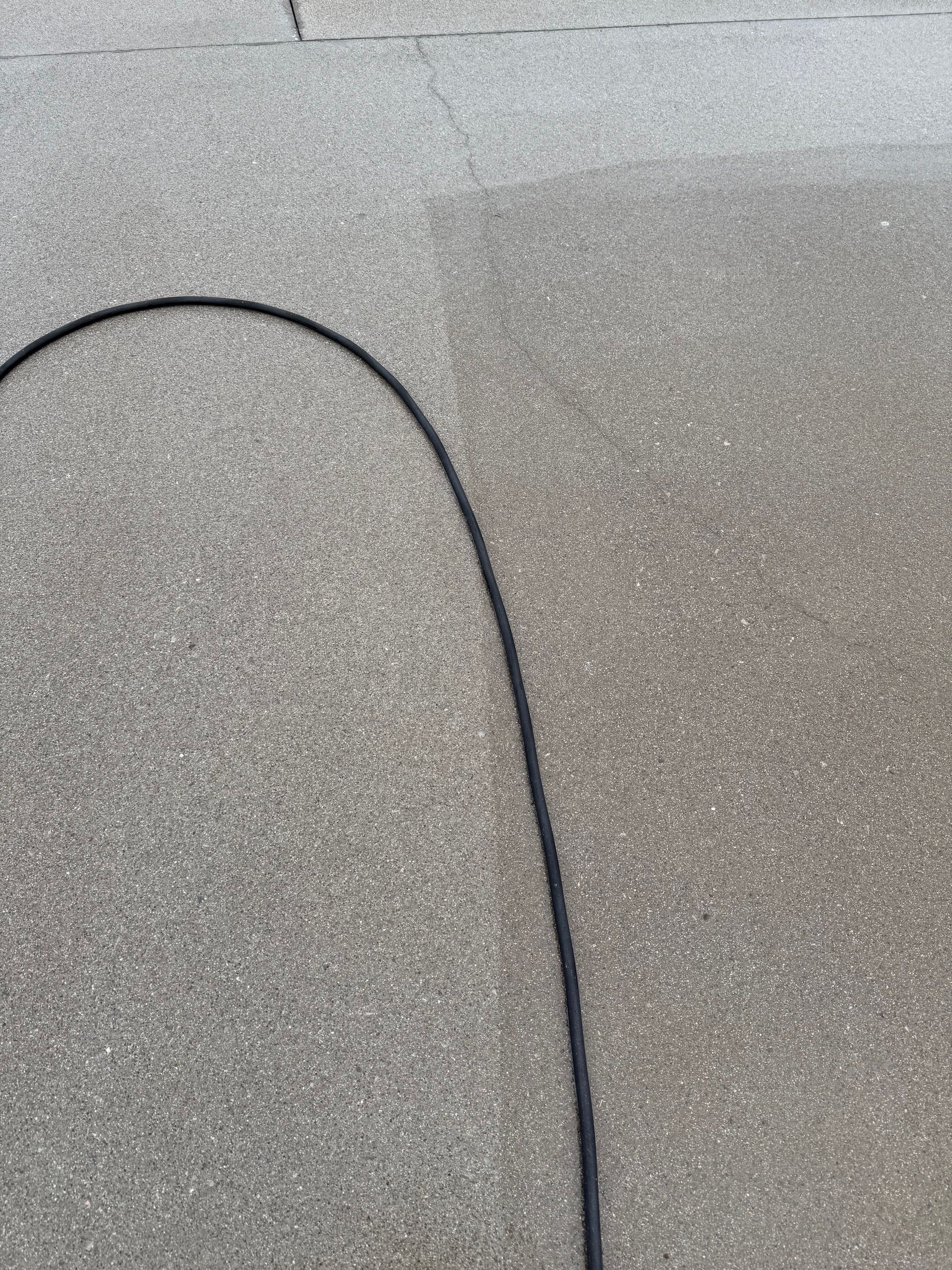 Black cable curving on gray concrete.