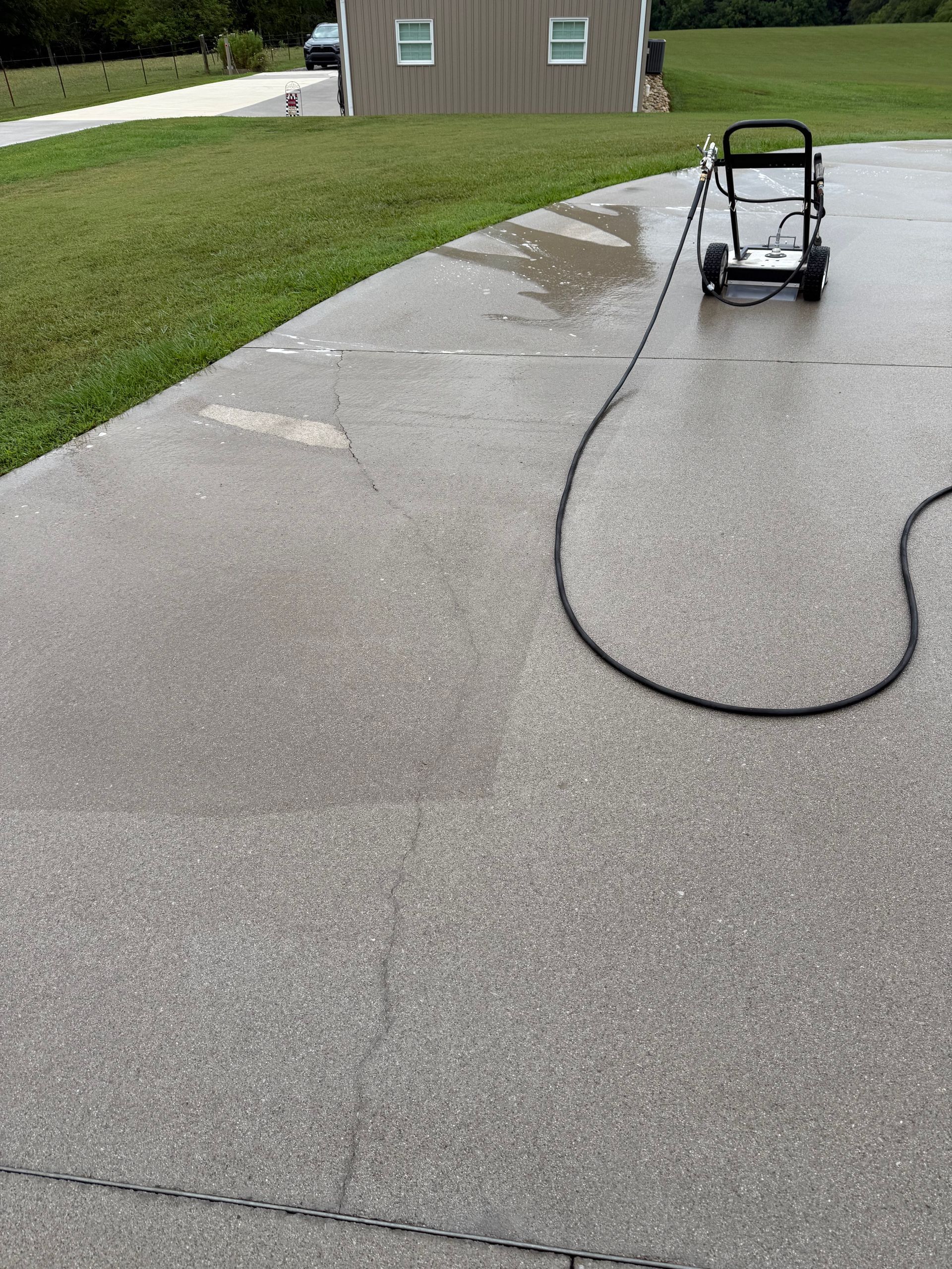 Pressure washer cleaning a wet concrete driveway.