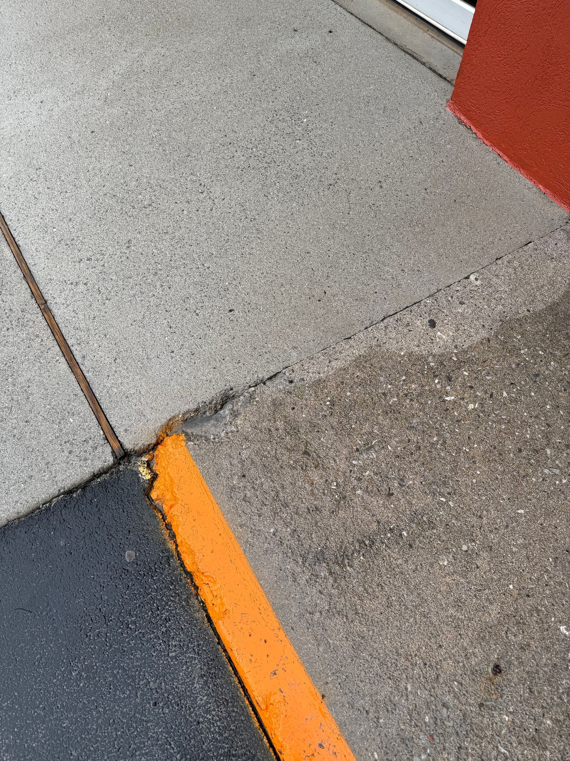 Gray concrete sidewalk with black asphalt and orange line, next to a red wall.