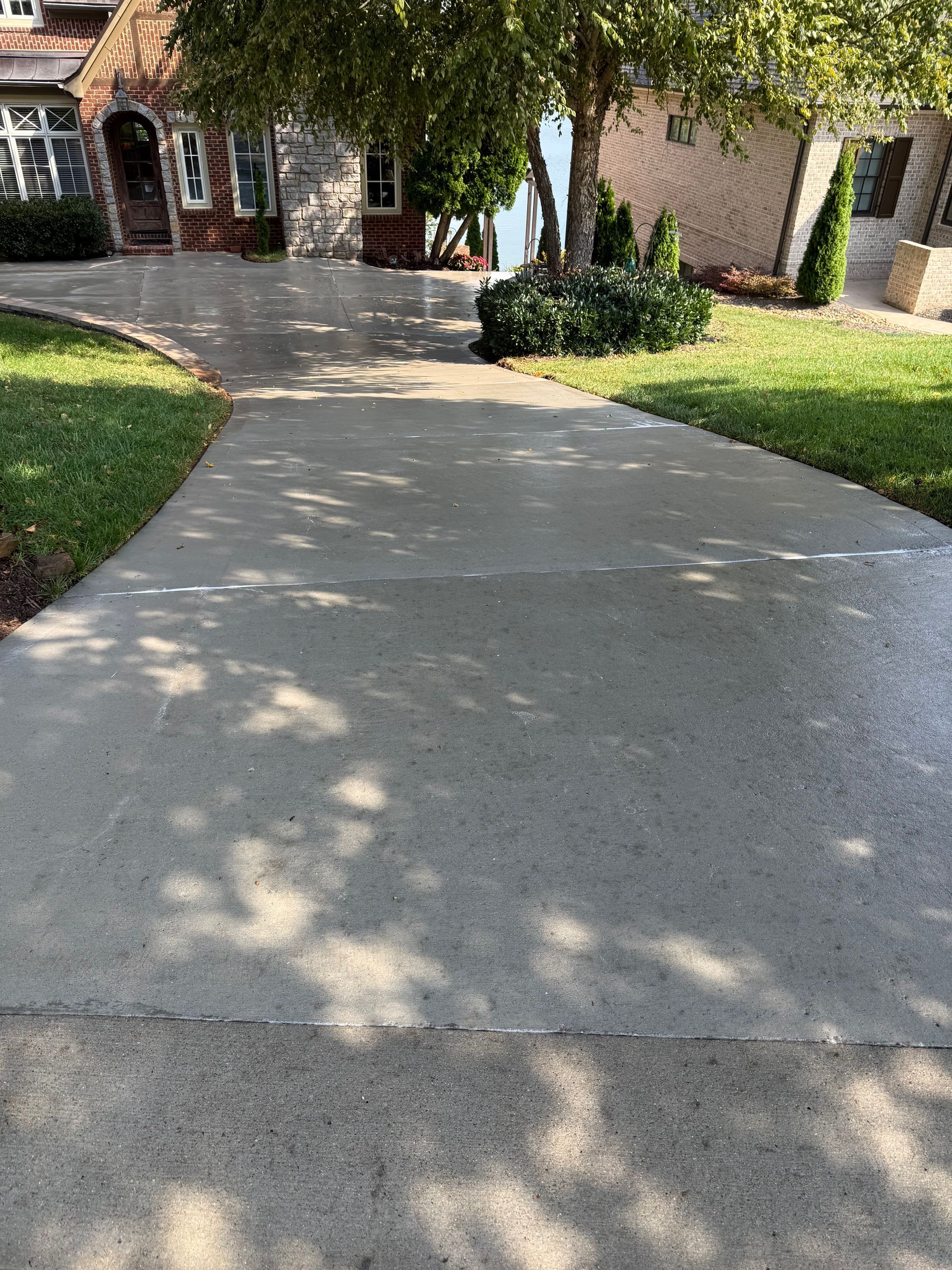 Gray concrete driveway with a house in the background and a tree casting shadows.