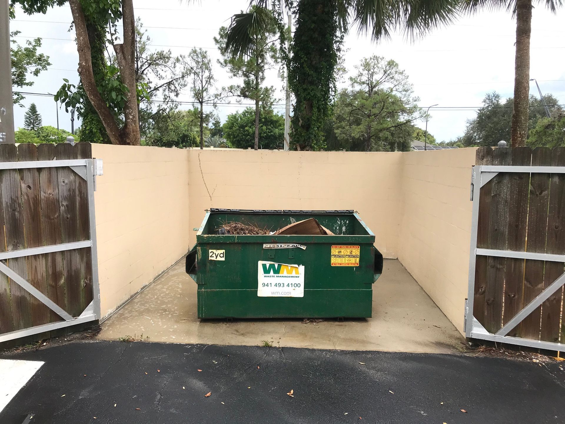 A green dumpster is sitting in a fenced in area.