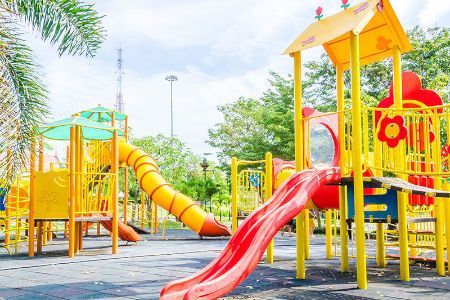 A colorful playground with a red slide and a yellow slide in a park.