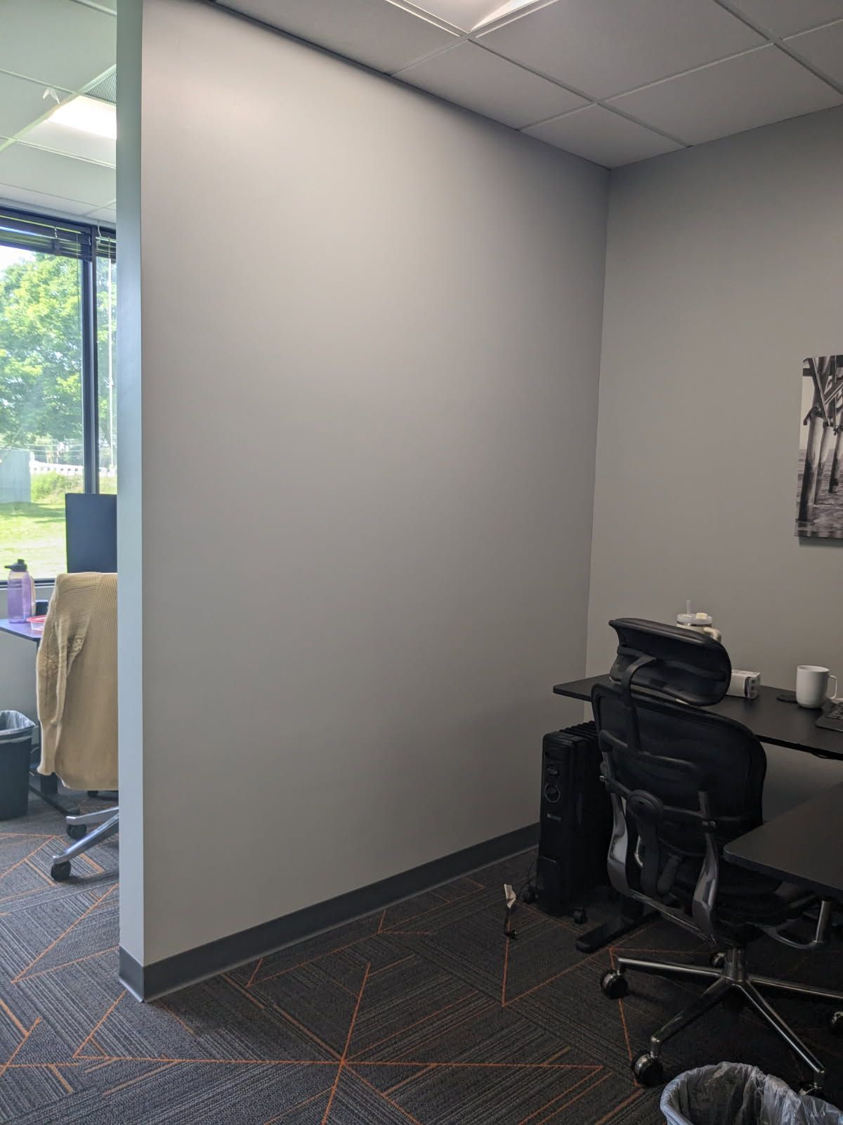 Empty office corner with gray walls, carpet, and a black office chair near a desk.