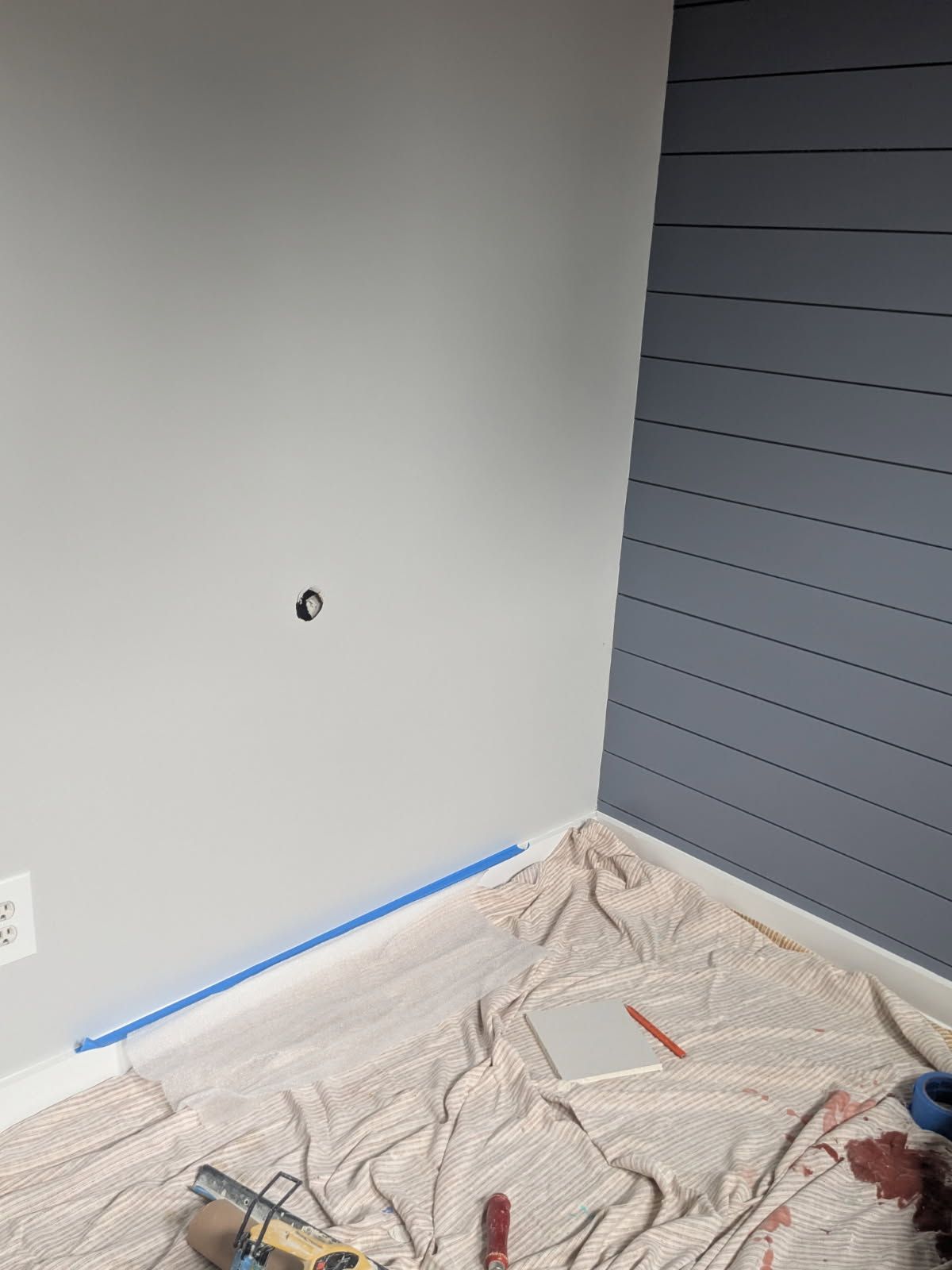 Painted room wall with taped baseboard, drop cloth on floor, and tools for painting prep