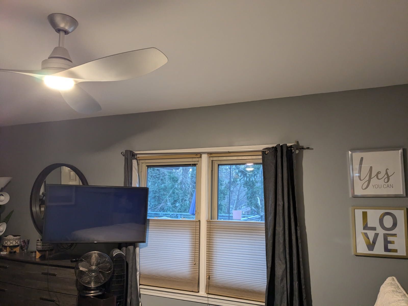 Living room with ceiling fan, TV on dresser, window blinds, and wall art reading “Yes” and “LOVE.”