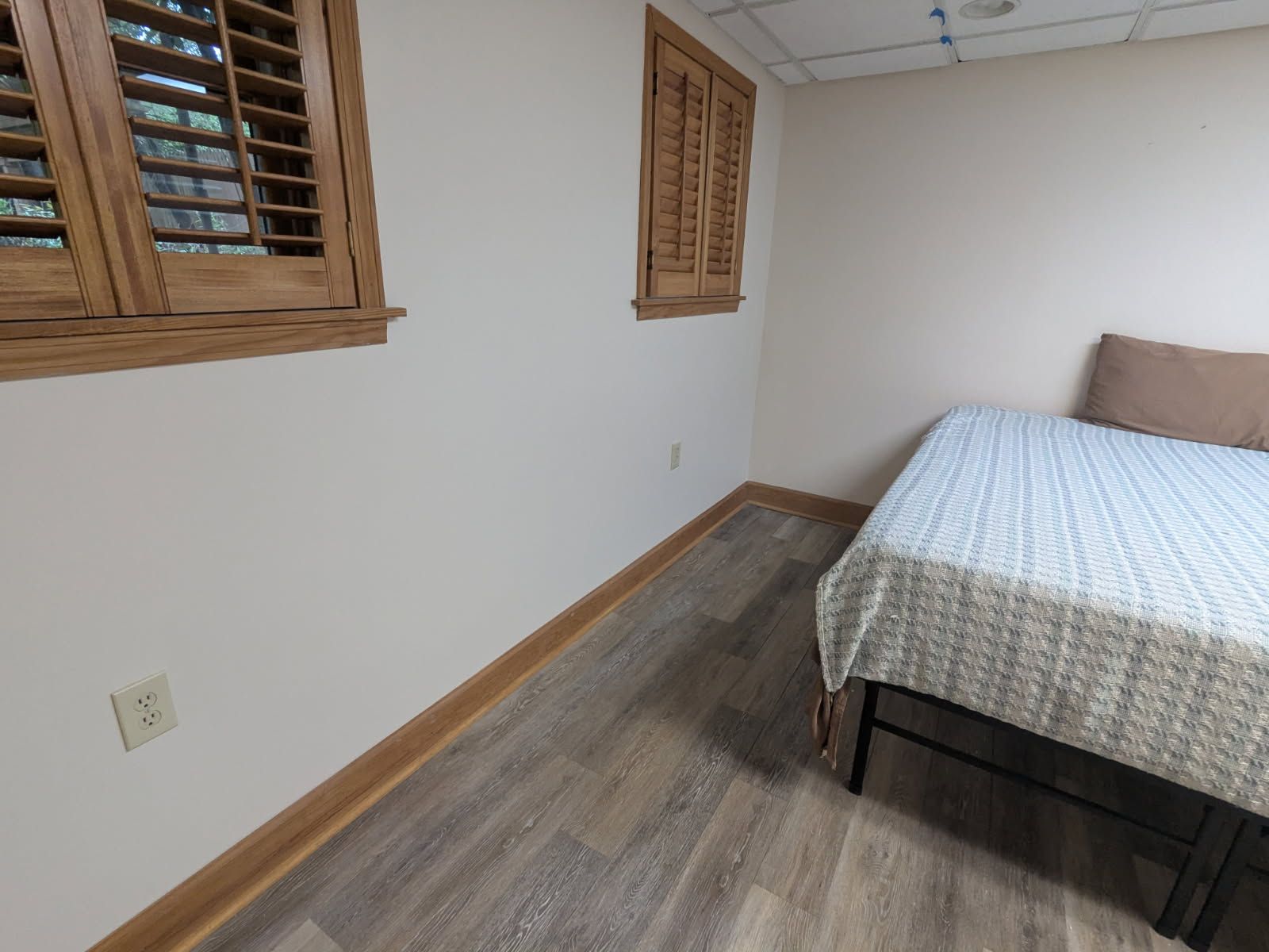 Small bedroom with a bed, wood-trimmed windows, and beige walls