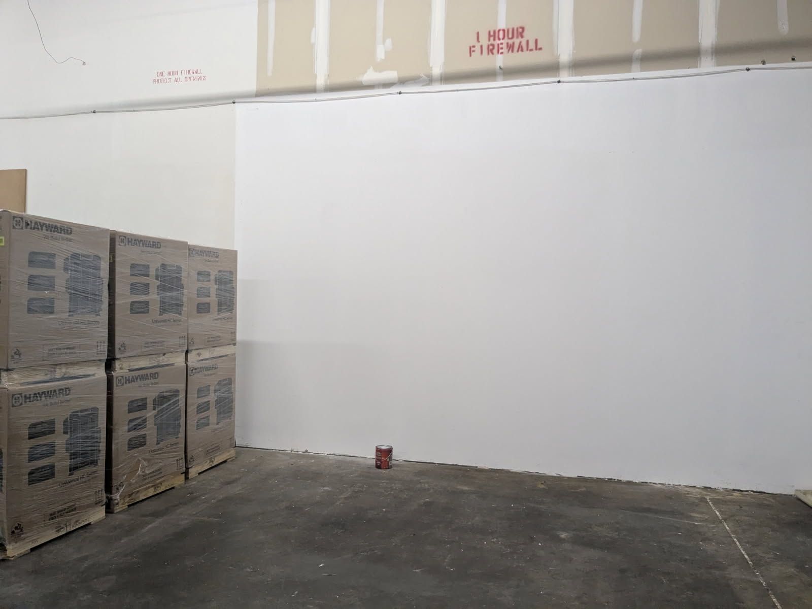 Empty warehouse corner with stacked cardboard boxes on the left and a small can on the floor.