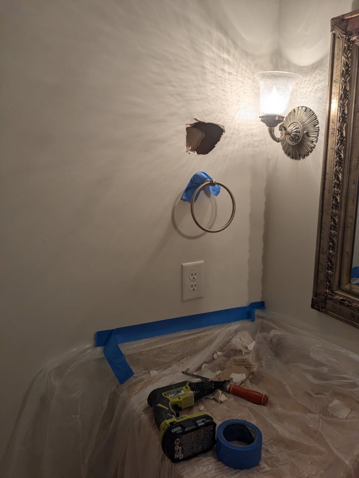 Bathroom wall with a patched hole, exposed wiring, and blue painter’s tape covering a sink area.