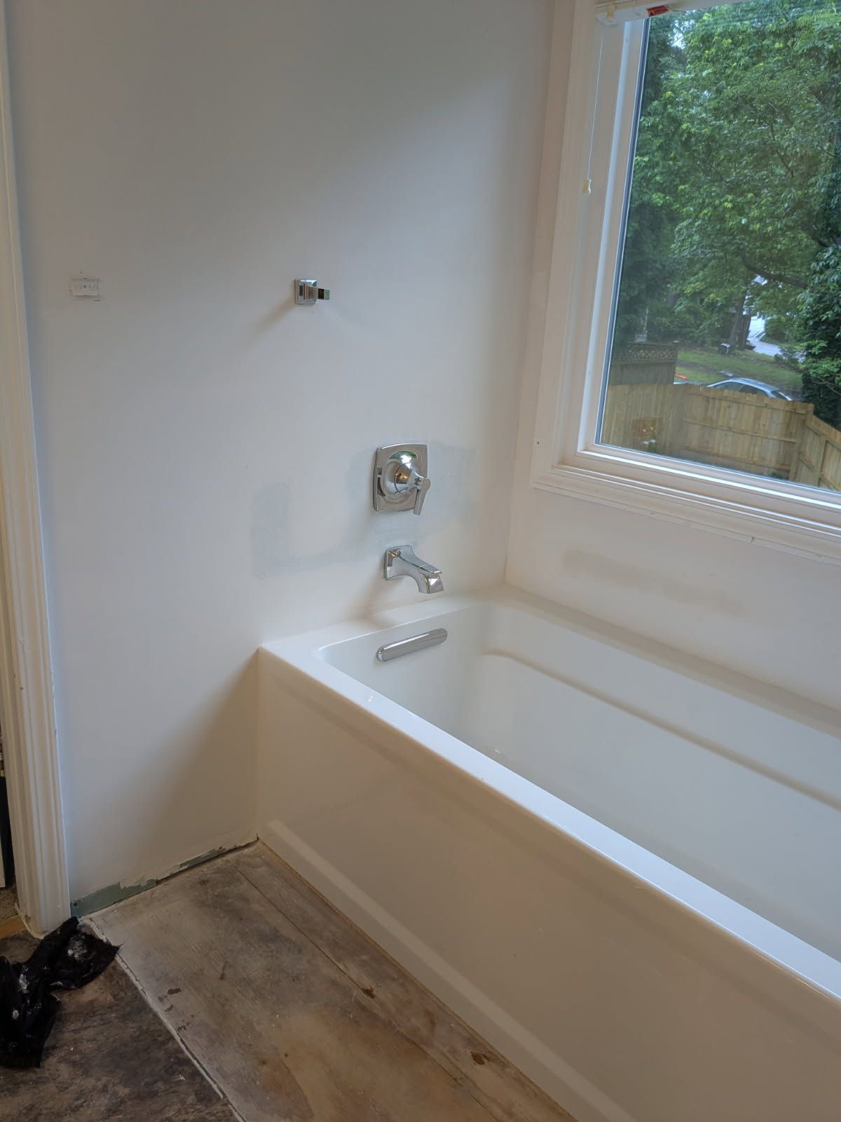 Bathroom with a white bathtub beside a window and tiled floor by the wall