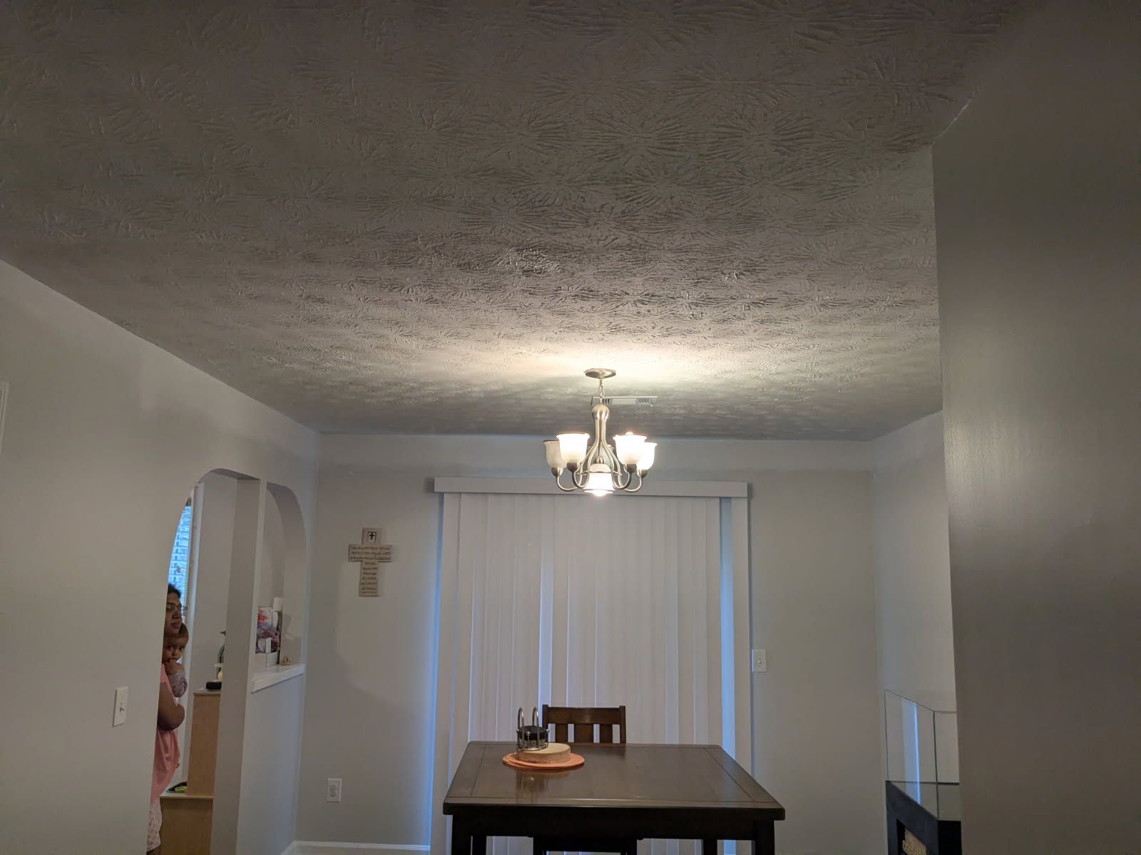 Dining room with a chandelier, wooden table, and white blinds in a modest hallway setting