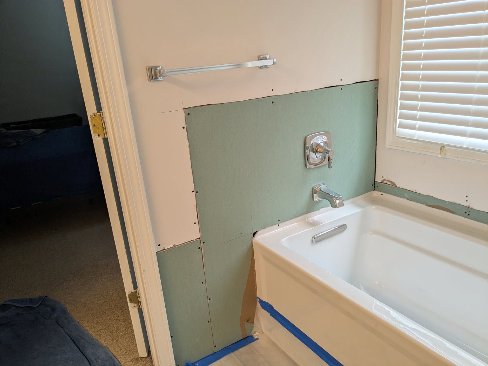 Bathroom with a bathtub under repair, exposed green drywall, and a towel bar above the tub