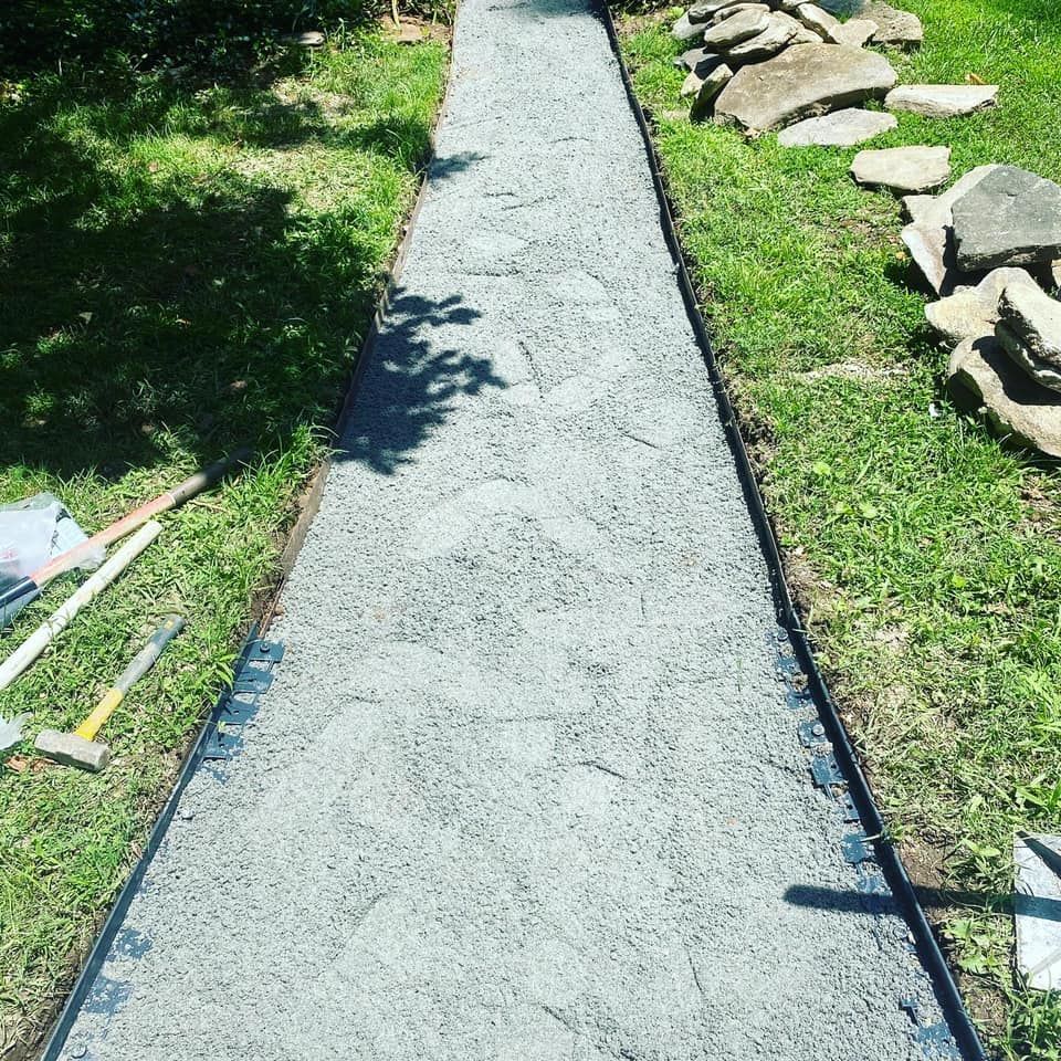 A straight, newly installed gravel garden path bordered by black landscape edging, flanked by lawn and scattered stones.