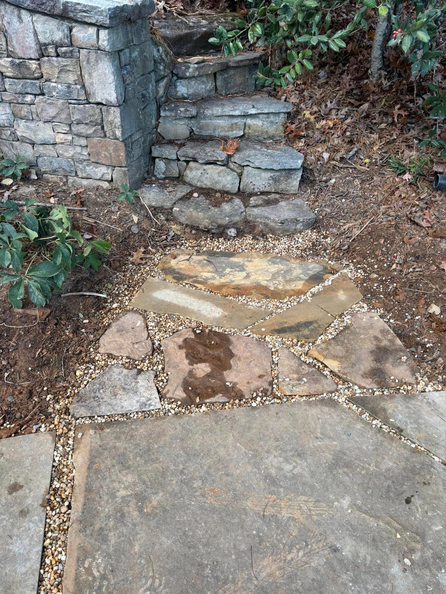 Stone steps and a paved path beside a retaining wall and dry leaves in a garden area