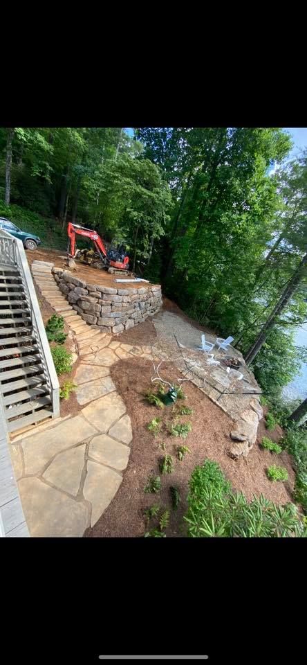 Steep outdoor hillside path with stone steps, dirt garden bed, and an orange excavator near trees
