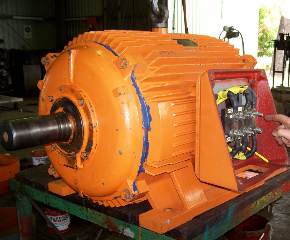 Orange industrial electric motor on a green table, open wiring access, indoors.— Davidson's Electrical In Central Highlands, QLD