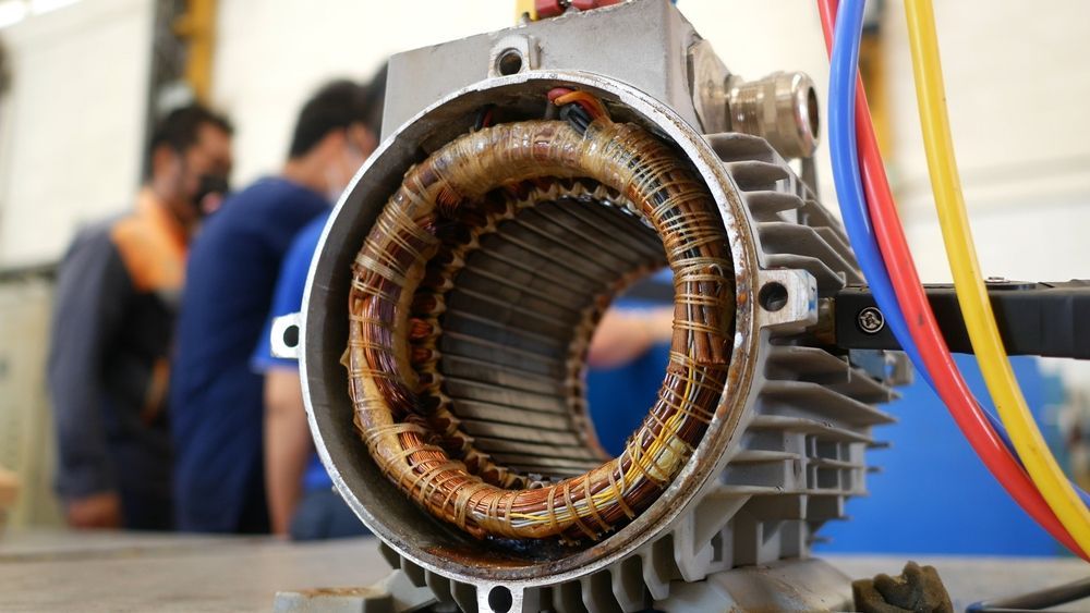 Open electric motor with copper windings, viewed close-up.  Men in the background— Davidson's Electrical In Parkhurst, QLD