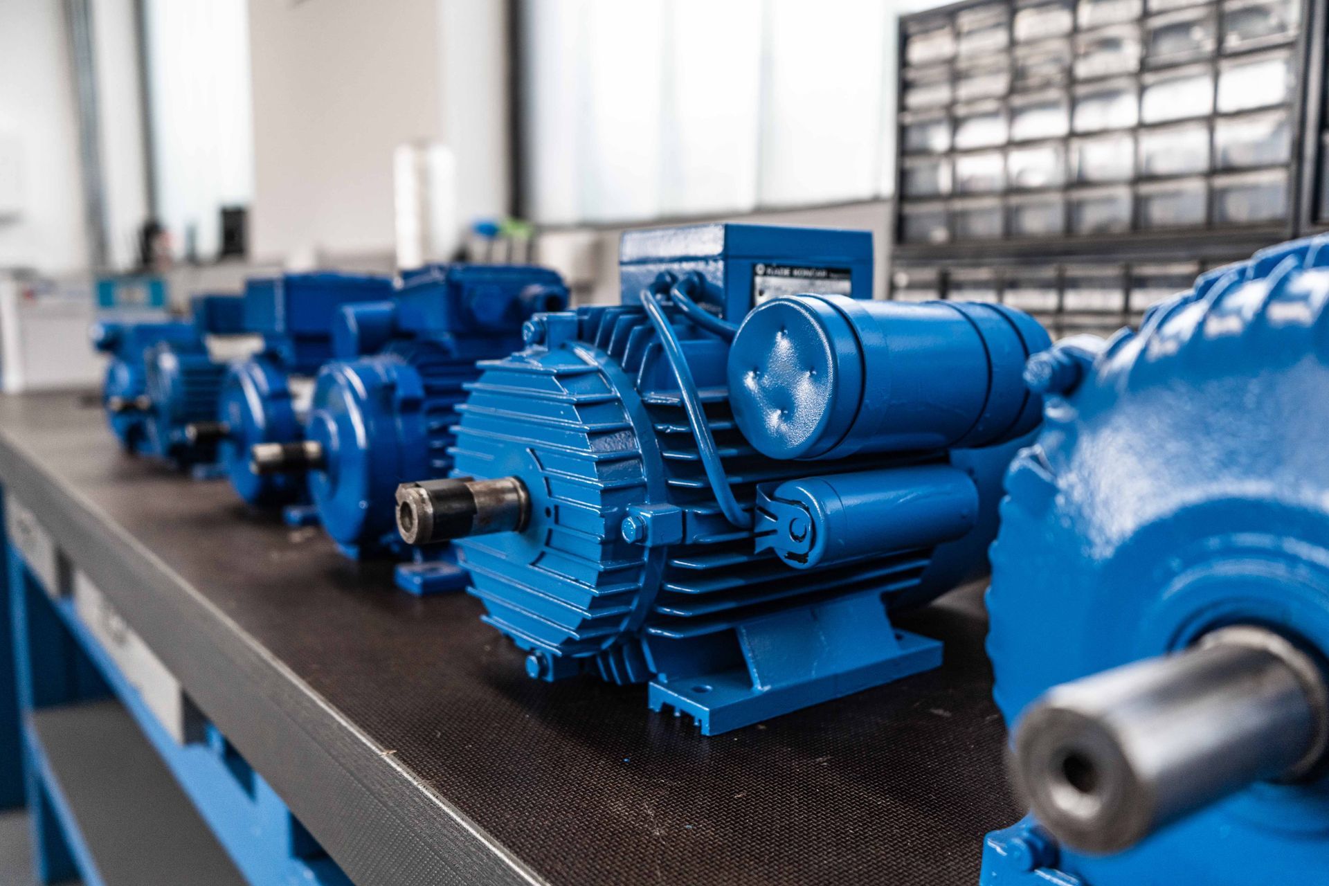 Blue electric motors lined up on a workbench in a workshop setting— Davidson's Electrical In Parkhurst, QLD