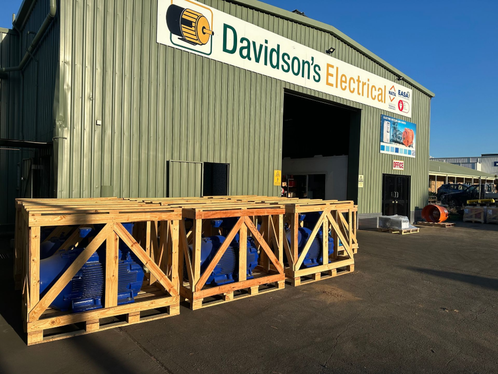 Three blue machinery crates outside a building with the sign
