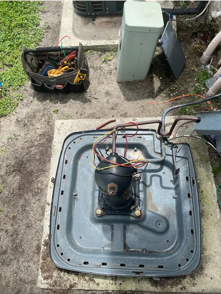An open AC unit with exposed compressor and toolbox nearby, outdoors.