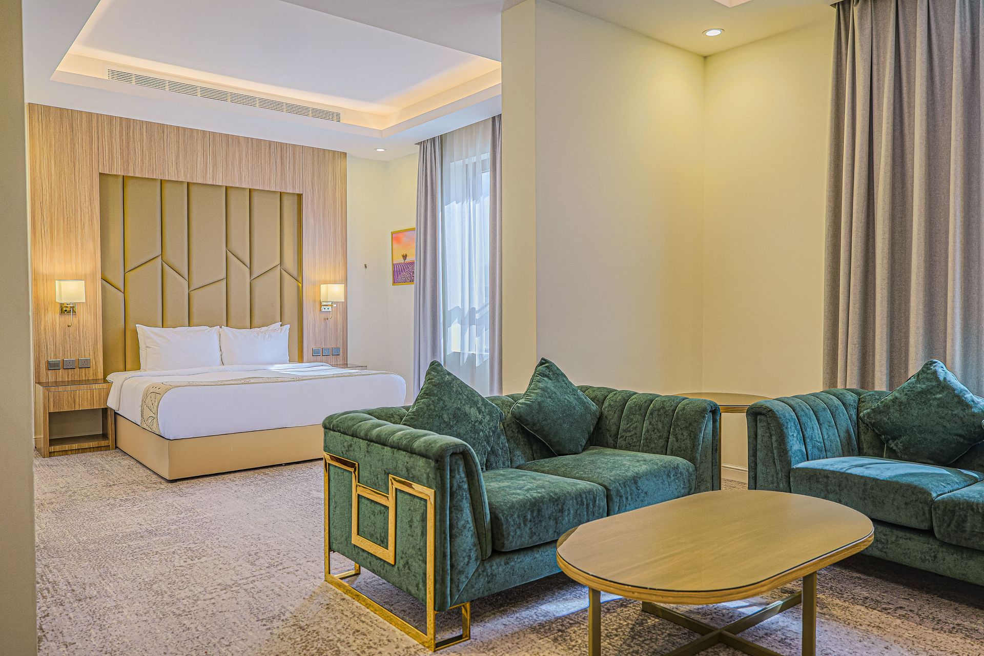 Modern hotel suite with king bed, teal sofa, and gold-trimmed coffee table
