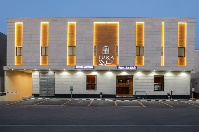 A modern two-story building with white horizontal panels, wooden window accents, and a central black entrance door.