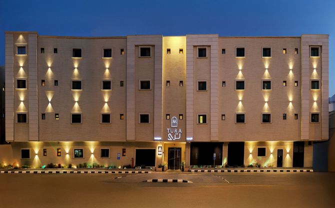A tan stone hotel building illuminated by exterior wall sconces at twilight, featuring a central entrance.