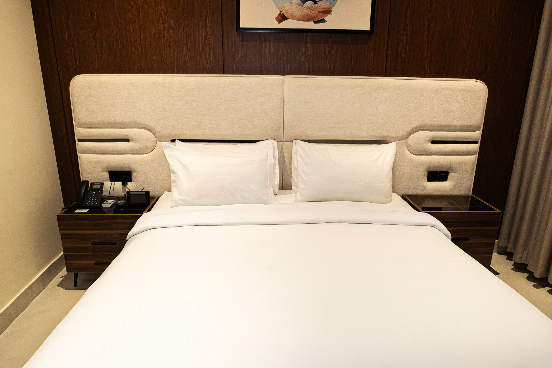 Neatly made white bed with pillows in a modern hotel room with wood-paneled walls and bedside tables
