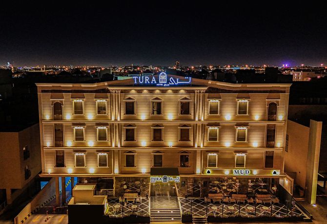A multi-story hotel building illuminated at night with warm golden lights, featuring an illuminated sign at the top.