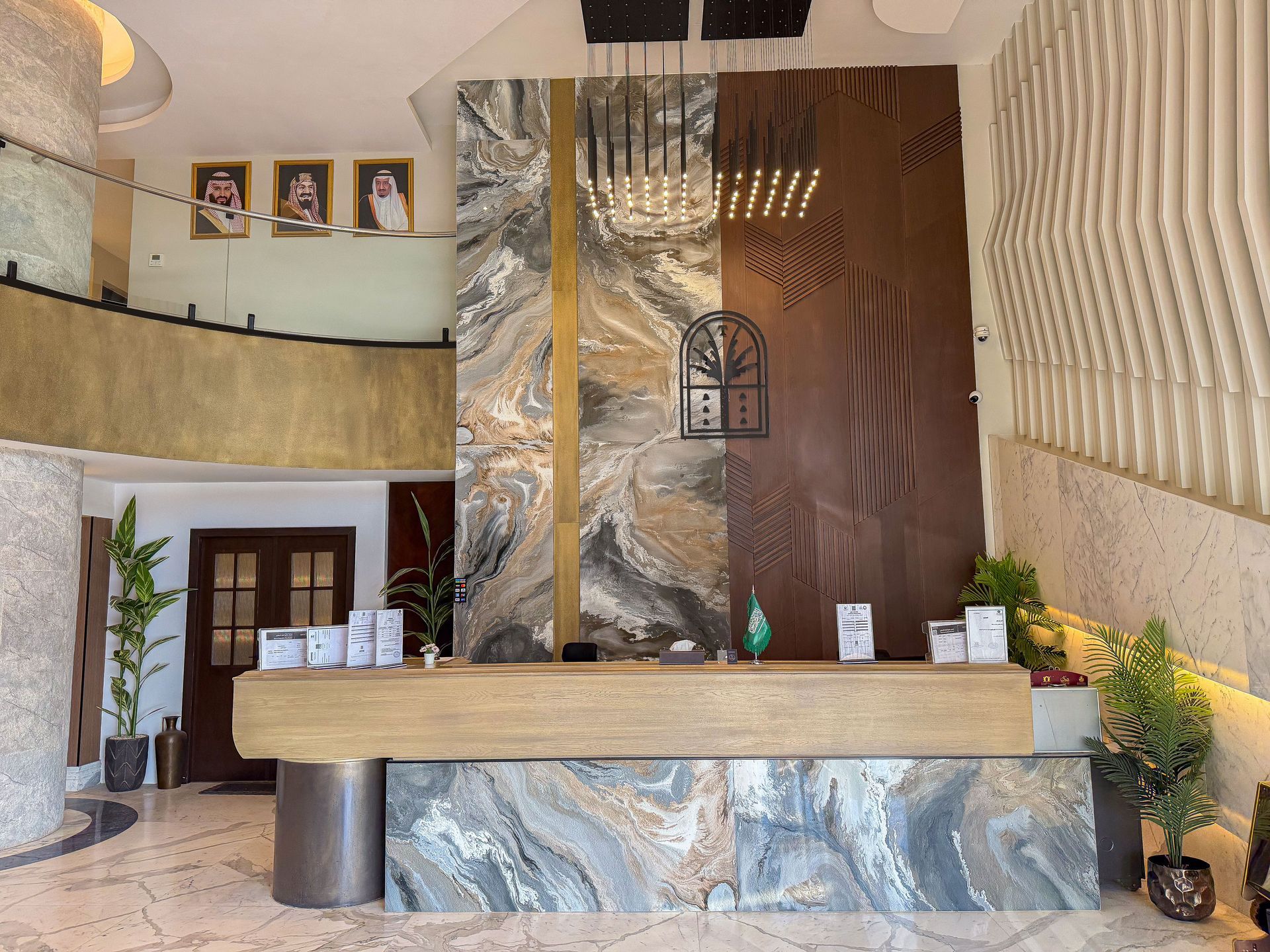 A hotel lobby with a large marble front desk, a dramatic feature wall, tiered lighting, and decorative plants.