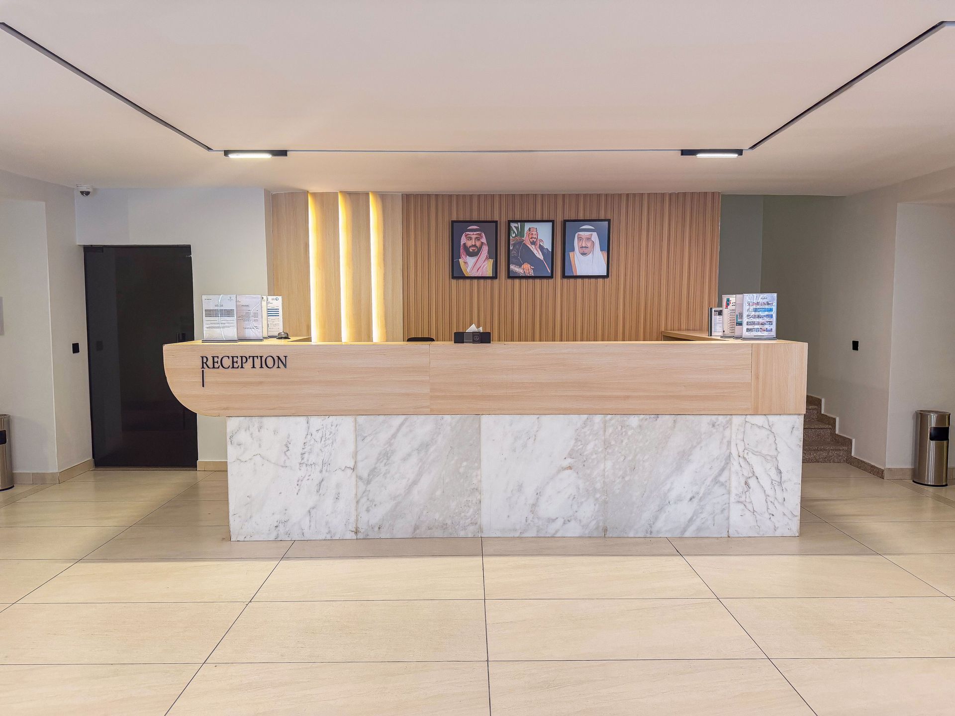 Modern hotel reception desk with white marble base, light wood counter, and three framed portraits on a wood-slat wall.