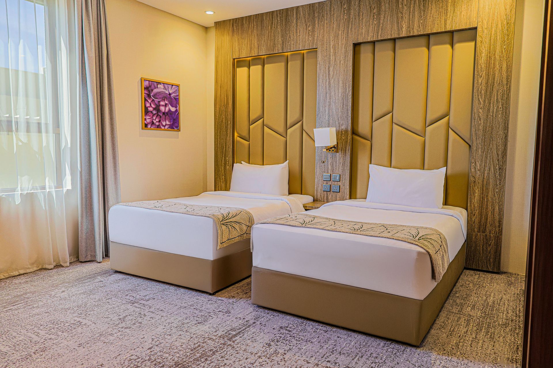 A hotel room featuring two twin beds with white linens, tan upholstered headboards, and patterned carpet flooring.